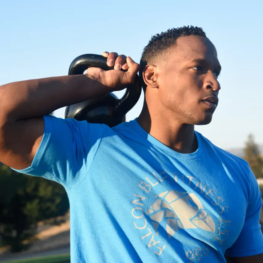 Coach Venchie pressing a kettlebell in a Falcon Blue Fitness tee